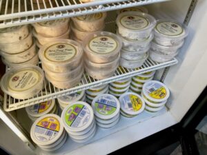 Vegan cream cheese options in the cooler at Balsam. Flavors shown are spicy veggie, chocolate chip, vegetable, plain, herbs & chives, and garlic & herb.
