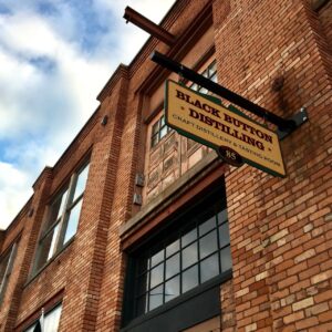 Front brick entrance to Black Button Distilling with a sign above the door