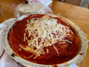 Takeout container of a vegan eggplant parm dish topped with vegan cheese.