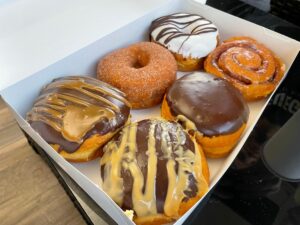 Half a dozen vegan donuts, including cinnamon sugar, boston cream, white frostings, and coffee cream.